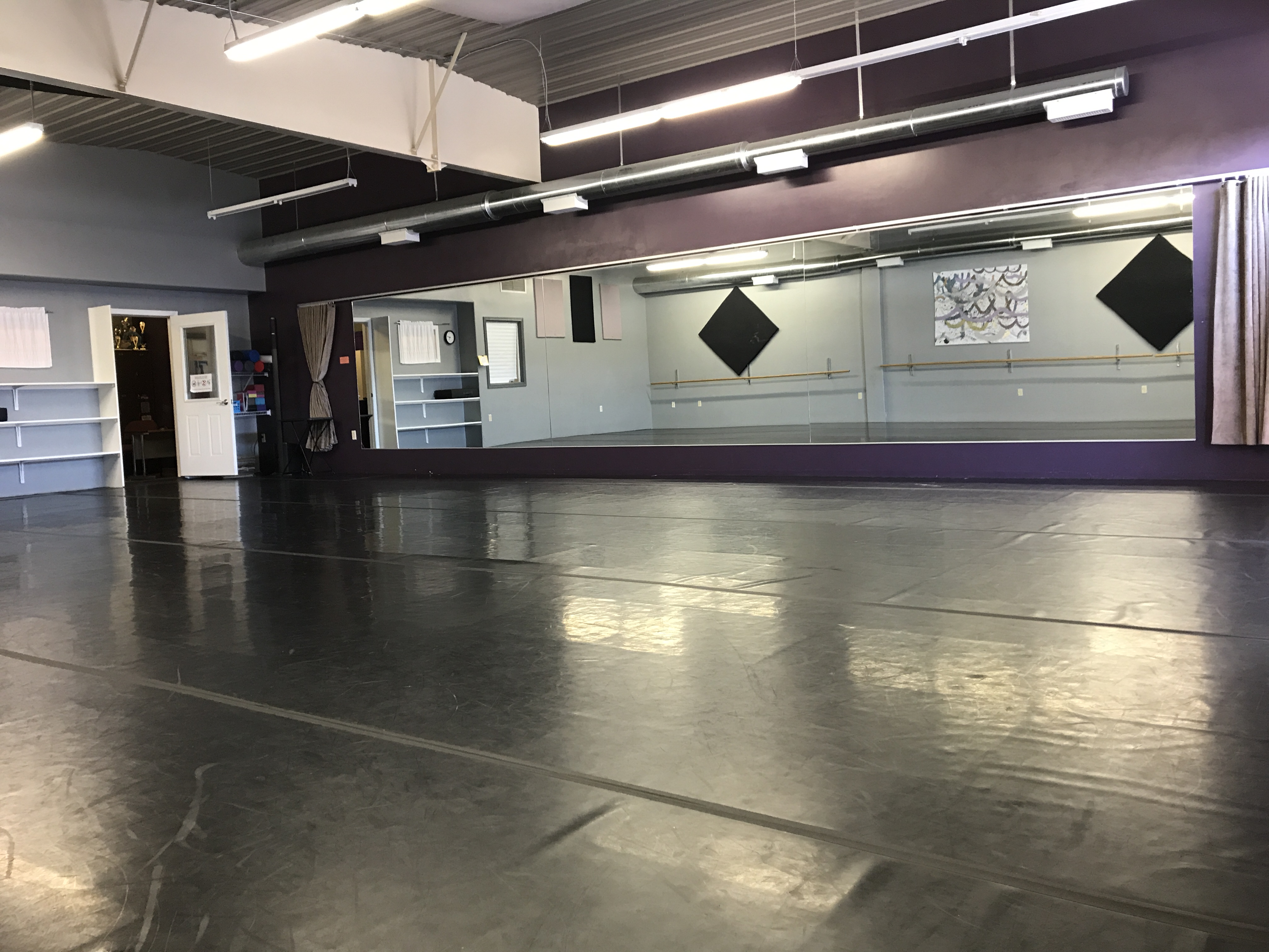 A dance studio with black marley, showing full length mirrors and a sound system.